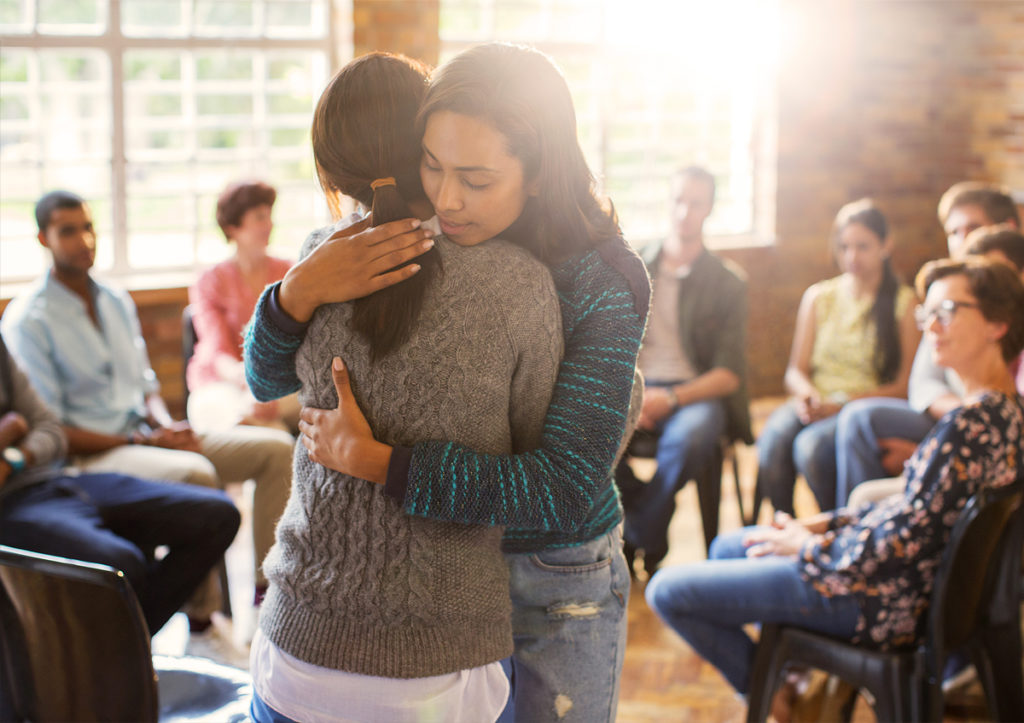 Women hugging in group therapy session.