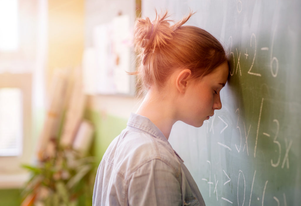 Depressed teenager girl leaning against a blackboard
