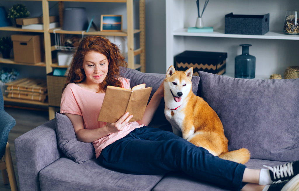 Young woman on sofa with dog. Best dog for apartment.