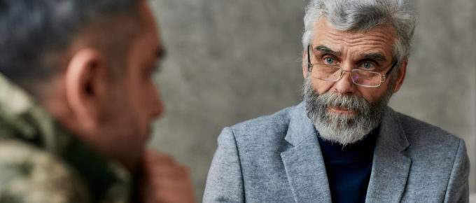 Portrait of mature psychologist communicating with military man during therapy session