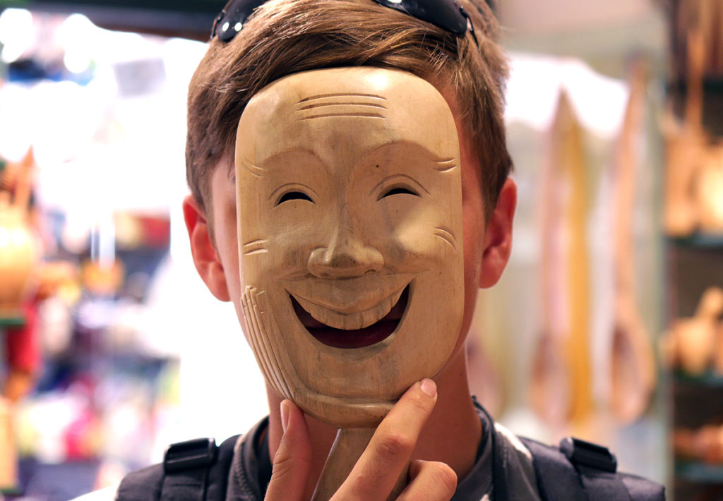 Man wearing a wooden mask with a fake smile